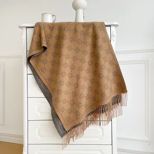 Detail of coffee cashmere scarf showing clover pattern and long tassel fringes on white cabinet