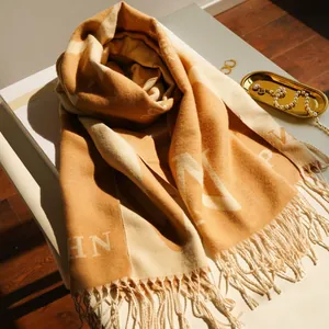 Thick cashmere-like scarf with large letter patterns and tassels in orange and beige