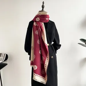 Detail view of double-sided camellia pattern scarf with tassels on a black coat