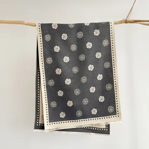 Elegant dark grey camellia jacquard scarf with fringe hanging on a rustic wooden branch