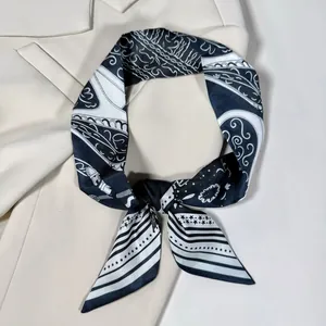 Dettaglio di un foulard in seta paisley bianco e nero annodato su un blazer beige