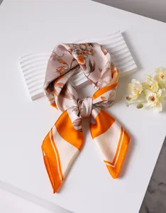 Close-up of silk scarf with orange floral print draped on a white textured display