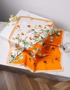 Detail of elegant orange silk square scarf with floral print on marble surface