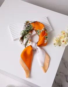 Detail of silk scarf tied in a bow with orange floral pattern and soft sheen finish