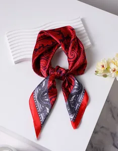 Détail d'un foulard en soie à motif cachemire rouge et violet sur fond texturé blanc