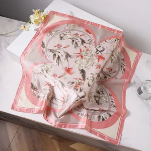 Elegant lily floral print silk scarf with pink edges displayed on marble surface