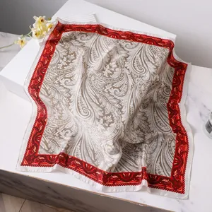 Carré de soie élégant à motif paisley taupe avec bordure rouge sur marbre blanc