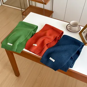 Solid color wool knitted scarves in green, orange, and blue on a cozy tabletop
