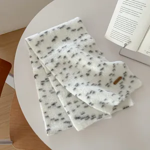 Dettaglio di sciarpa in maglia bianca a pois neri con etichetta in pelle su un tavolo