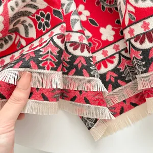 Detailed close-up of ethnic floral jacquard pattern and white fringe on a red thick scarf