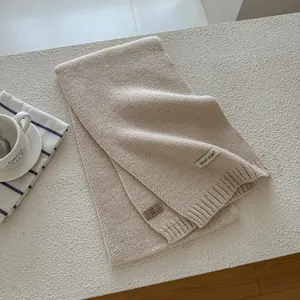 Detail of oat beige wool knit scarf showing fiber texture and composition care label