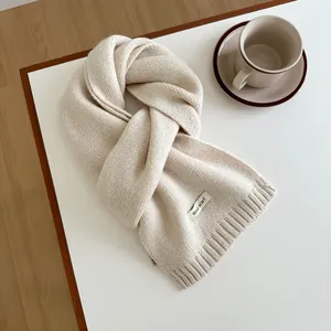 Close-up of beige wool knitted scarf with rib knit edges and a decorative brand tag