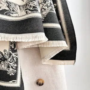 Macro detail of black and white floral pattern shawl with tassel fringe on beige coat