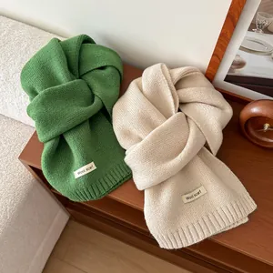 Close-up of thick knitted wool scarves in green and beige with minimalist brand tags