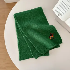Dettaglio della morbida sciarpa in maglia verde con ricamo di cane carino e trama soffice
