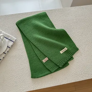 Detail showing the green knitted wool scarf texture with material label and ribbed edge