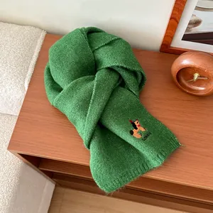 Dettaglio sciarpa in maglia verde erba con ricamo a cucciolo su tavolo di legno