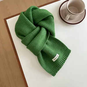 Detailed close-up of a vibrant green wool knitted scarf on a minimalist table