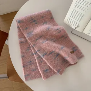 Dettaglio della sciarpa in maglia rosa e blu con etichetta in pelle su un tavolo