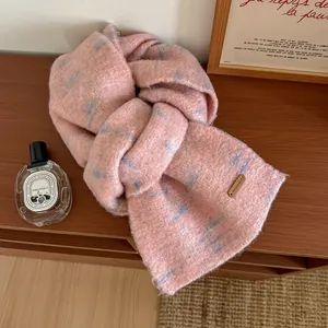 Dettaglio di sciarpa in lana sfumata rosa e blu con placchetta in metallo su tavolo di legno