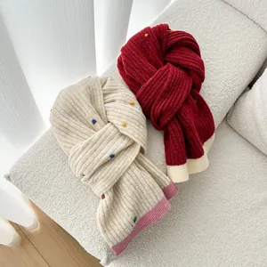 Knitted wool scarf with colorful pom-poms in cream and burgundy colors on a soft sofa