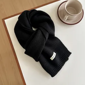 Macro detail of black wool scarf featuring thick knit texture and white woven label