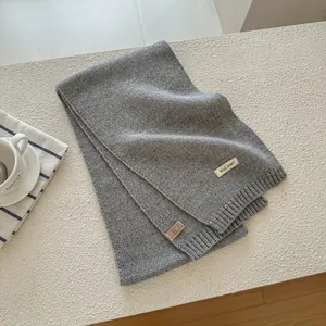 Detailed close-up of light grey wool blend knit scarf texture and material label