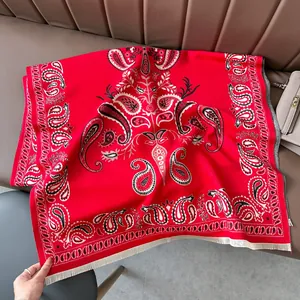 Red paisley cashmere shawl with white fringe details on a brown leather sofa