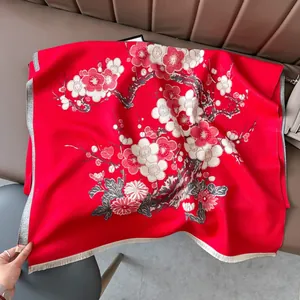 Dettaglio macro della sciarpa rossa con fiori di prugno e nappe in finta cashmere