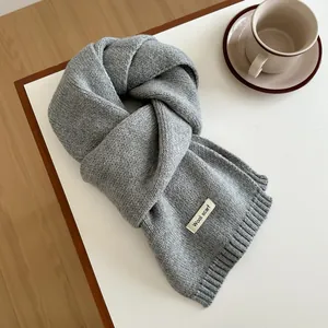 Detail of grey wool scarf texture with minimal woven label on wooden surface