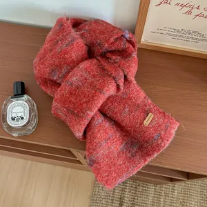 Dettaglio della sciarpa in maglia di lana rossa con texture morbida e placca dorata