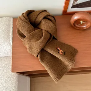 Dettaglio di sciarpa in maglia marrone scuro con ricamo cucciolo su superficie legno