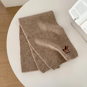 Dettaglio di sciarpa in maglia marrone con ricamo di cane carino e testo cutedog