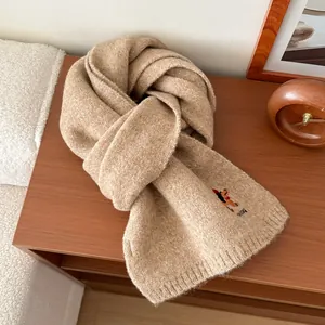 Dettaglio ravvicinato della sciarpa in maglia beige con ricamo cucciolo e logo tedog