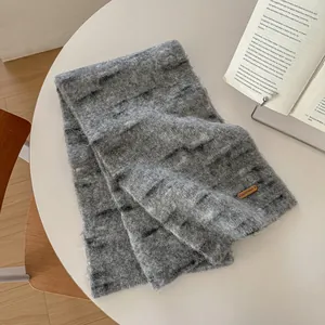 Dettaglio di sciarpa grigia in maglia di lana con texture mohair e logo in pelle