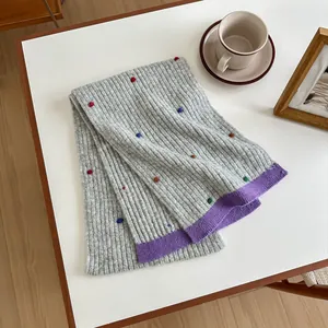 Detail of grey knitted wool scarf with colorful pom poms on a cozy home desk setting