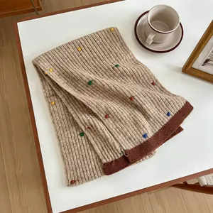 Detail of beige ribbed knit wool scarf featuring multi-color specks and contrast brown border