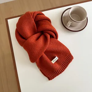 Detailed view of an orange wool knit scarf with ribbed edges and white branded label