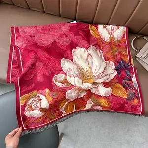 Gros plan sur un châle rouge en cachemire avec motif jacquard floral et pompons gris