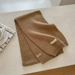 Detailed shot of camel wool blend knit scarf with woven label on soft textured background