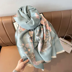 Dettaglio scialle pashmina azzurro con motivo floreale rosa e frange su divano in pelle