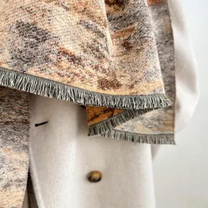 Detalle de bufanda con motivo de pintura al óleo terroso y flecos suaves sobre abrigo blanco
