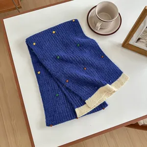 Detail of royal blue knit scarf featuring colorful dot accents and cream contrast hem