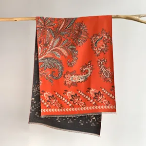 Detail of orange and grey paisley scarf with fringe on a wooden branch background