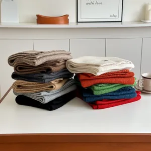 Close-up of soft knitted wool scarves in multiple colors stacked on a white surface