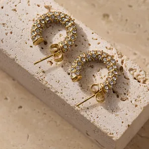 Vue macro de boucles d'oreilles en C dorées 18k avec strass brillants et perles