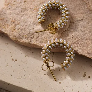 Détail de boucles d'oreilles en C plaqué or 18k avec perles sur un fond de roche