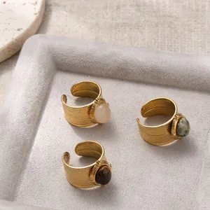 Detailed view of 18K gold plated wide rings with colorful gemstones on a gray tray