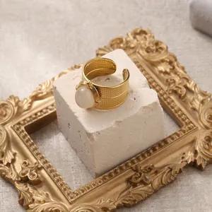 Detail of adjustable gold ring featuring white gemstone and woven texture on stone background