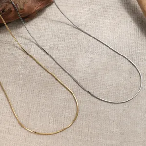 Close-up of gold and silver snake bone necklaces on a textured natural fabric